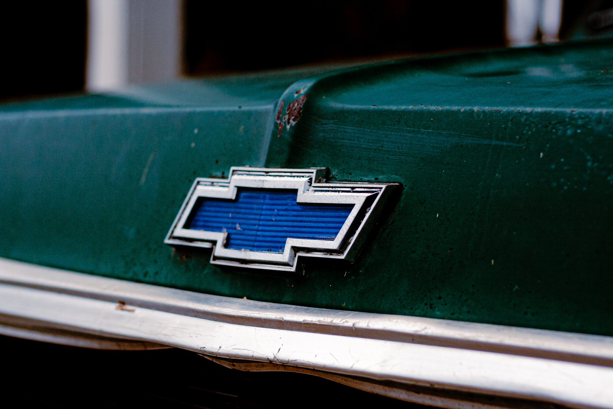 Photograph of the emblem of a Chevrolet truck, taken at an angle. In the background, the garage is slightly visible.